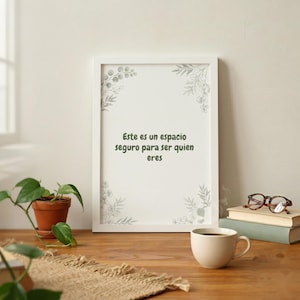 May include: A white framed wall art print featuring the Spanish text "Este es un espacio seguro para ser quien eres" in dark green lettering, accented by delicate, light green botanical illustrations of leaves in each of the four corners.