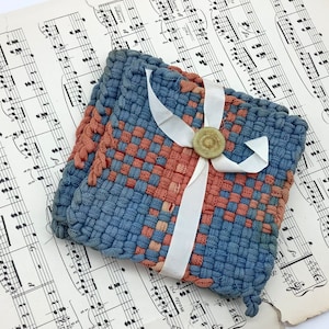 May include: Two blue and red woven fabric coasters with a white ribbon tied around them and a small round button in the center. The coasters are sitting on a sheet of music.