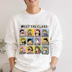 Op de afbeelding: Witte sweatshirt met een kleurrijke afbeelding met de tekst "MEET THE CLASS" en cartoonillustraties van verschillende studentenarchetypen, waaronder "The Yapster", "The Gamer" en "The Last Minute Homework Kid".