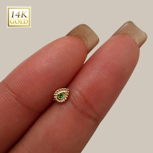 Könnte beinhalten: Ein goldfarbener, tropfenförmiger Ohrstecker mit einem kleinen, runden grünen Edelstein in der Mitte. Der Ohrring ist von einem Perlendesign umgeben. In der oberen linken Ecke des Bildes befindet sich ein goldenes Quadrat mit dem Text "14K GOLD".