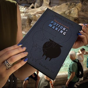 Può includere: Un libro blu scuro intitolato "BORAGE'S Advanced POTION-MAKING" con un'illustrazione di un calderone nero. Il libro ha una copertina strutturata e il testo "Edition IV". Lo sfondo mostra una fontana e delle persone.