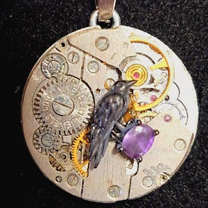 May include: A silver pendant necklace featuring a detailed raven perched on a purple gemstone. The pendant is crafted from a repurposed watch mechanism, showcasing intricate gears and a vintage aesthetic.