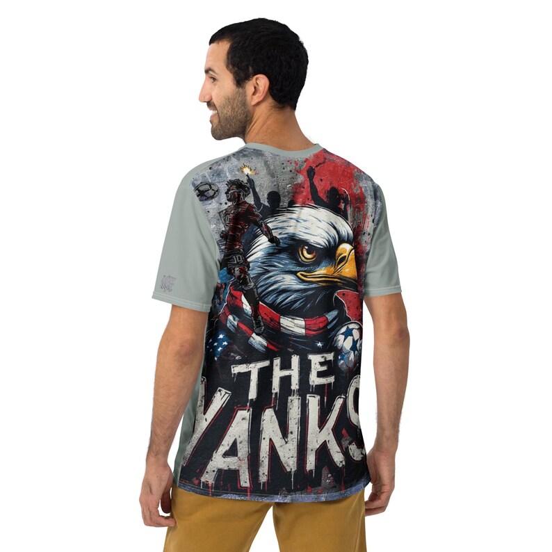 May include: A light gray t-shirt featuring a graphic of an American bald eagle with a red, white, and blue scarf. The text "THE YANKS" is displayed in bold, white letters. The shirt has a crew neck and short sleeves.