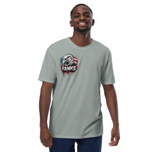 May include: A light gray t-shirt featuring a graphic of an eagle's head with the American flag and the word "Yanks" in red. The shirt is short-sleeved and has a crew neck.