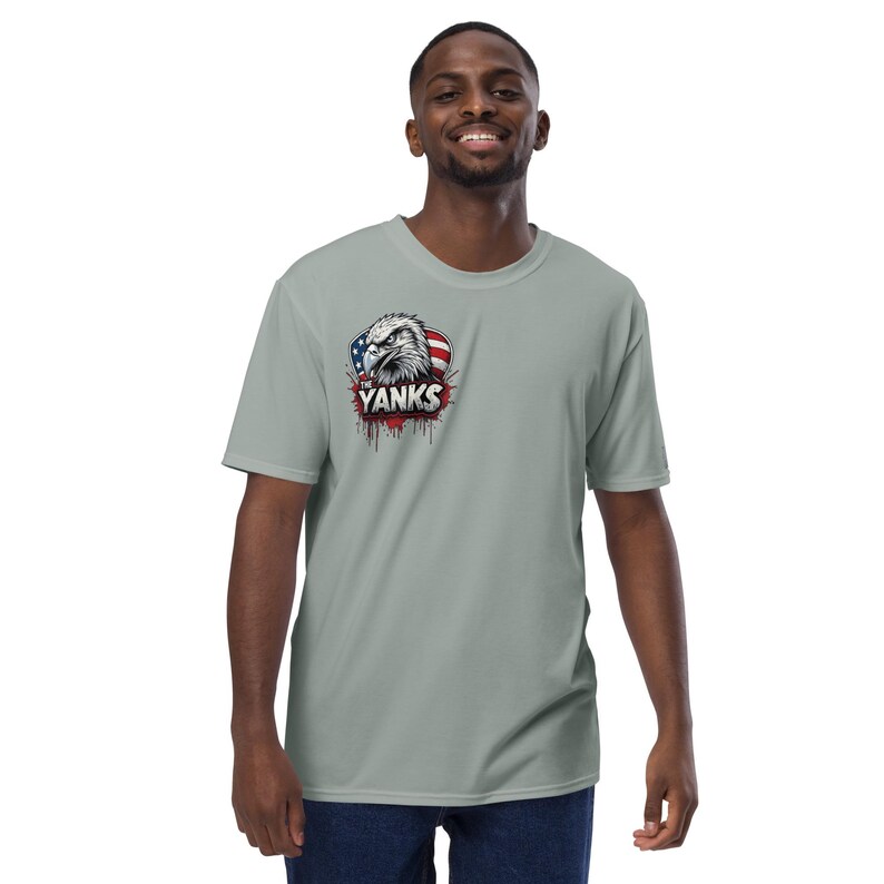 May include: A light gray t-shirt featuring a graphic of an eagle's head with the American flag and the word "Yanks" in red. The shirt is short-sleeved and has a crew neck.