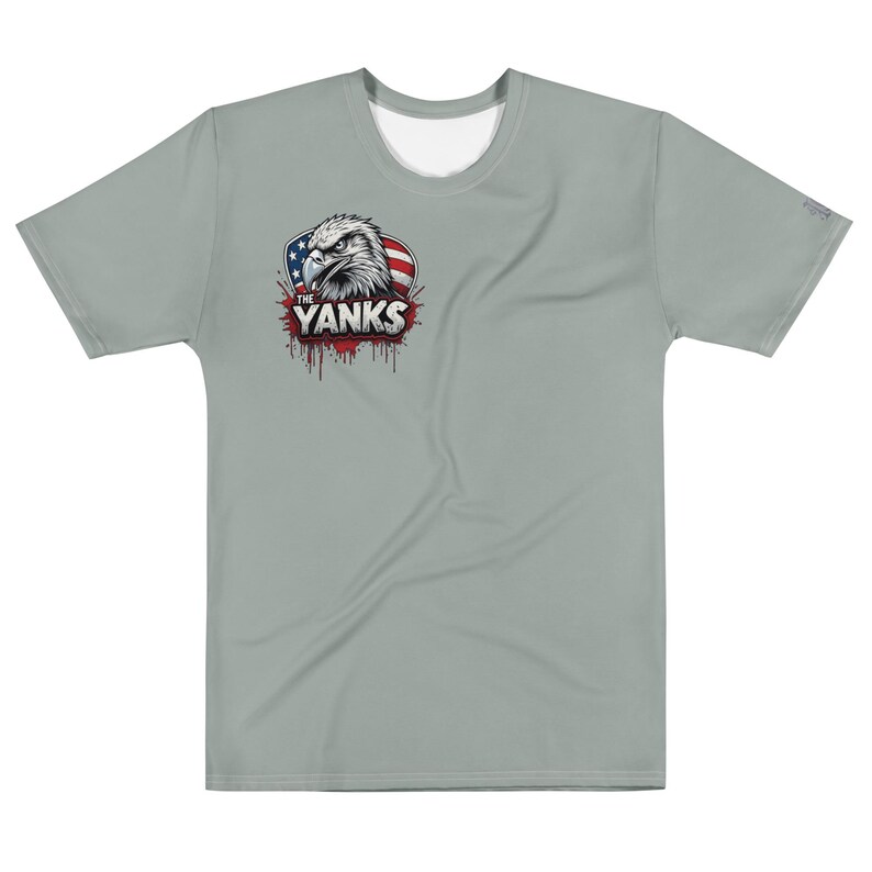 May include: A light gray t-shirt featuring a graphic of an eagle's head with the text "THE YANKS" and a red, white, and blue design. The shirt has short sleeves and a crew neck.