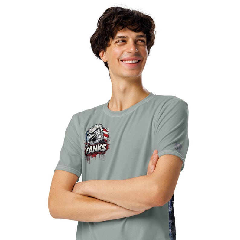 May include: A light gray t-shirt featuring a graphic of an eagle's head with the text "Yanks" and American flag accents. The shirt has short sleeves and a crew neck.
