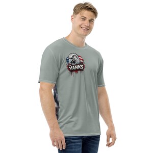 May include: A light gray short-sleeve t-shirt featuring a graphic of an eagle with the American flag and the text "Yanks". The shirt has a patterned design on the side.