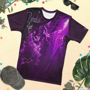 May include: A purple t-shirt with the words "Paradise Lost" in white script. The shirt features a vibrant, abstract design in shades of purple and black. The sleeves are a solid dark purple color.