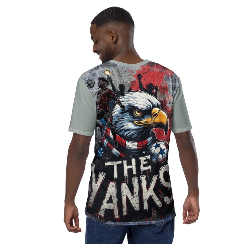 May include: A light green t-shirt featuring a graphic of a bald eagle with a red, white, and blue scarf. The text "THE YANKS" is below the eagle. Soccer balls and silhouettes of soccer players are also visible.