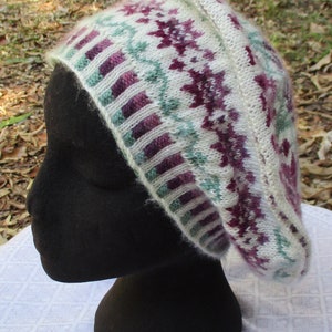 May include: A white, purple and green knitted beanie with a geometric pattern. The beanie is displayed on a black mannequin head.