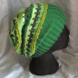 May include: A green and brown knitted beanie with a striped pattern. The beanie is on a black mannequin head.