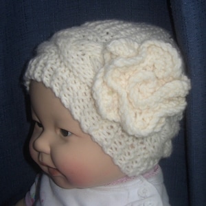 May include: A white knitted baby hat with a large flower detail on the side.