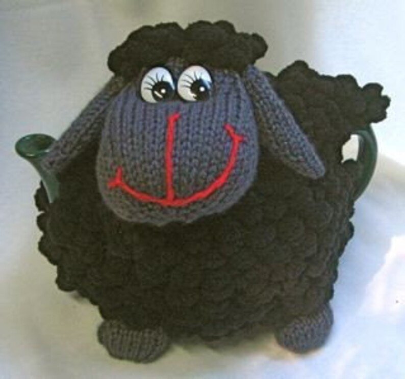 May include: A black knitted teapot cozy shaped like a sheep with large eyes and a red smile.