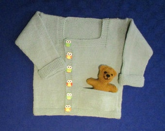 May include: A light green knitted cardigan with a square neckline and a pocket on the front. The cardigan has a row of owl buttons down the front and a small teddy bear in the pocket.
