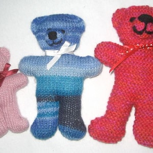 May include: Three knitted teddy bears in pink, blue and red. The pink bear has a red ribbon around its neck. The blue bear has a white ribbon around its neck. The red bear has a red and white ribbon around its neck.
