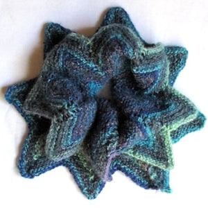 Puede incluir: Una bufanda de punto azul, verde y morado en forma de estrella. La bufanda está hecha de hilo suave y tiene un aspecto texturizado.