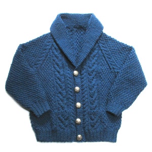 Peut inclure: Un cardigan bleu en tricot avec un large col et des boutons argentés. Le cardigan est à motif torsadé.