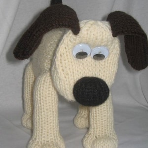May include: A knitted dog toy with brown ears and a black nose. The dog has large white eyes with black pupils.