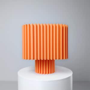 May include: An orange, modern lamp with a cylindrical shade and base, both featuring vertical ridged detailing. The lamp sits atop a white, cylindrical pedestal against a light gray backdrop.