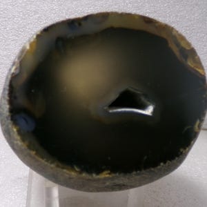 May include: A polished agate geode, showcasing a dark interior with a triangular opening. The outer edge is a mix of brown and tan, with a smooth, rounded shape. The geode's interior has a gradient of dark green and tan.