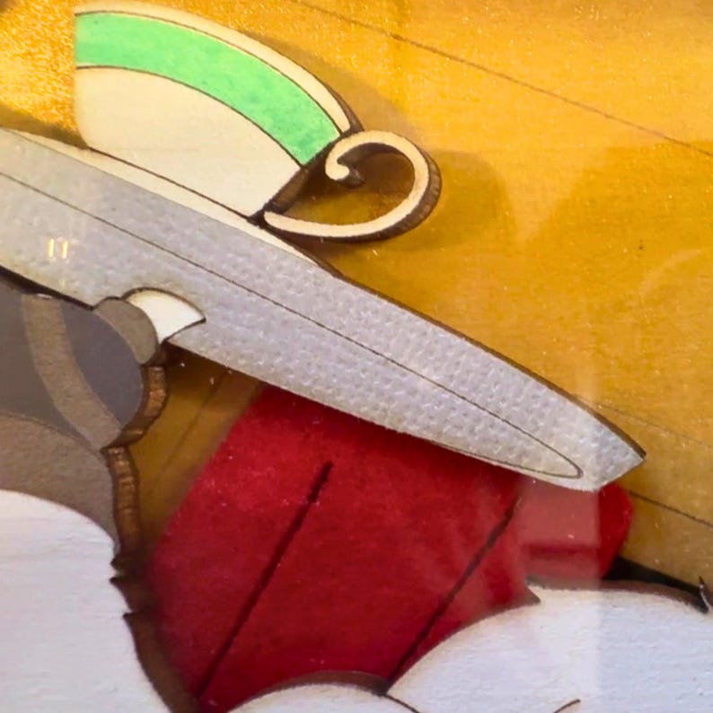 Puede incluir: Una pieza de arte mural de madera en capas que presenta una taza de t&eacute; blanca estilizada con una banda verde y un asa curva, colocada sobre una forma de hoja plateada texturizada, todo sobre un fondo amarillo vibrante con un acento rojo.