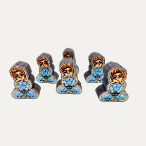 May include: A collection of wooden figurines depicting a person in a blue jumpsuit, seated in a meditative pose. The figurines have brown hair, sunglasses, and a gray hooded jacket. The base of each figurine is a dark gray color.