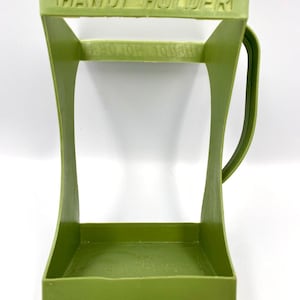 May include: A green plastic "HAND HOLDER" with a rectangular base, curved sides, and a handle. The text "HAND HOLDER" is embossed on the top. The object is designed to hold something.