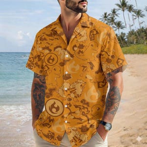 May include: Mustard yellow short-sleeve button-down shirt featuring a repeating pattern of cartoon characters and fire symbols. The shirt has a classic collar and is worn by a person on a beach.
