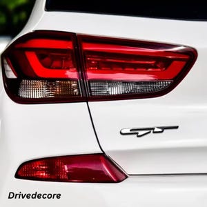 May include: Rear view of a white car featuring a red tail light and a black "GT" emblem. The tail light has a modern design. The text "Drivedecore" is visible at the bottom of the image.