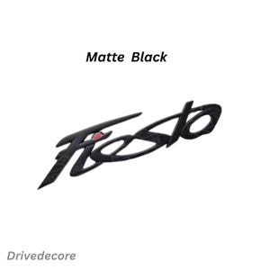 May include: Matte black "Fiesta" emblem with a red accent. The word "Fiesta" is in a stylized font. The text "Matte Black" is above the emblem, and "Drivedecore" is below.
