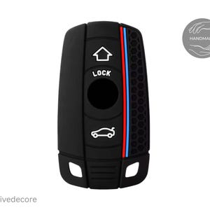 May include: Black car key cover with a red, blue, and white stripe design. The cover has a honeycomb pattern on the right side and features the words "LOCK" and car and house icons. The word "Handmade" is in a circle.