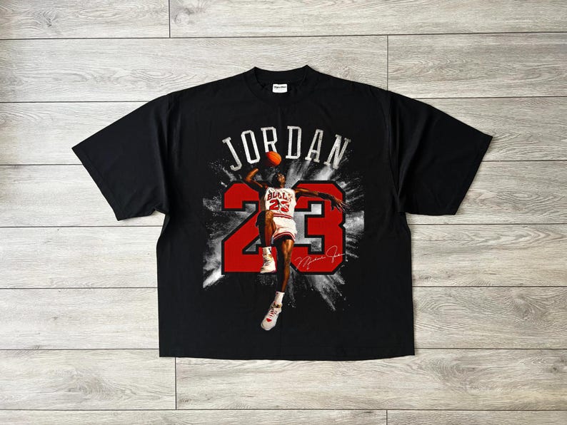 May include: Black t-shirt with a graphic of Michael Jordan in action, the word "JORDAN" above and the number "23" in red. Includes a signature. A classic basketball-themed garment.