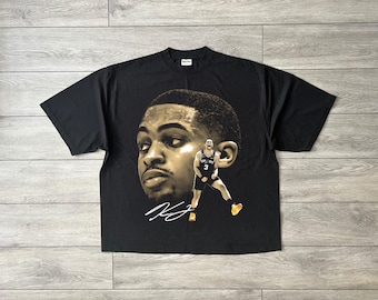 May include: Black t-shirt featuring a sepia-toned image of a basketball player's face and a smaller image of the player in action. The player is wearing a jersey with the number 3. A signature is below the face.