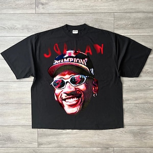 May include: Black t-shirt with a colourful portrait of a smiling person wearing sunglasses and a baseball cap with the word "Champions". The word "Jordan" is written in red above the portrait.