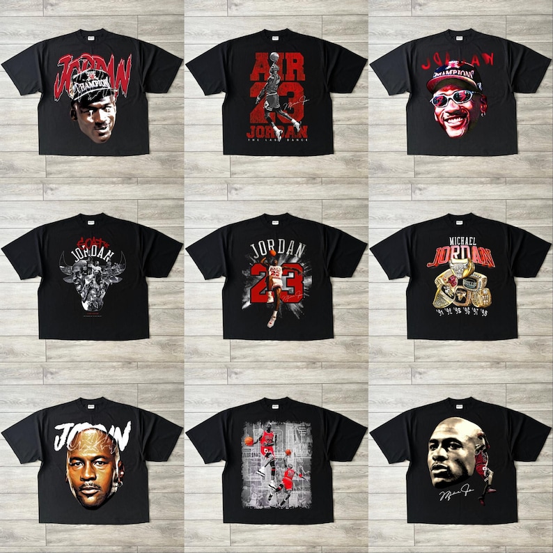 May include: Nine black t-shirts with different Michael Jordan graphics. Designs include portraits, action shots, and text such as "JORDAN" and "AIR 23". The shirts are displayed on a light-coloured surface.