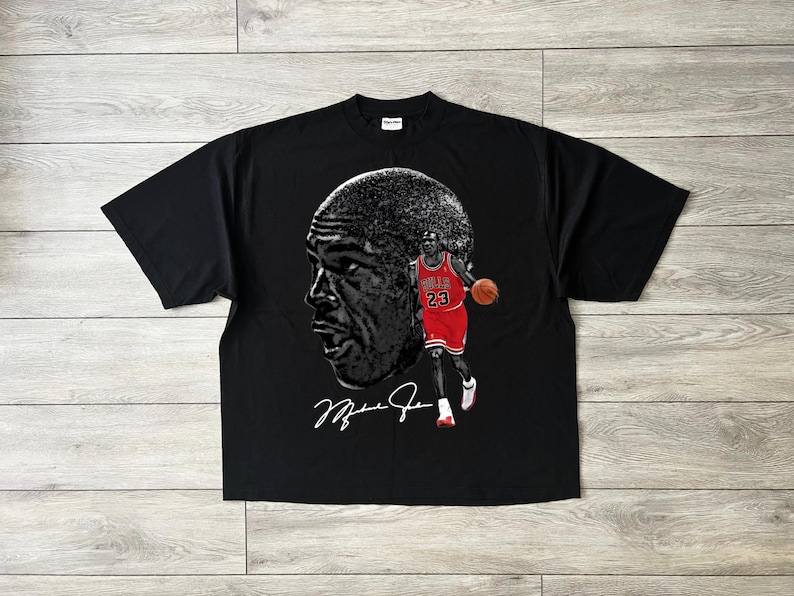 May include: Black t-shirt featuring a large grayscale image of a basketball player's face and a full-body image of the player in a red and black uniform. The player is holding a basketball. The shirt also has the player's signature.