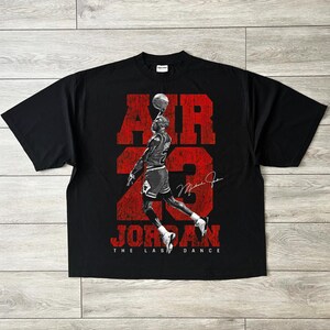 May include: Black t-shirt with a red graphic of a basketball player balancing a ball, with the words "AIR 23 JORDAN". The text "THE LAST DANCE" is below the player. The shirt has a crew neck and short sleeves.