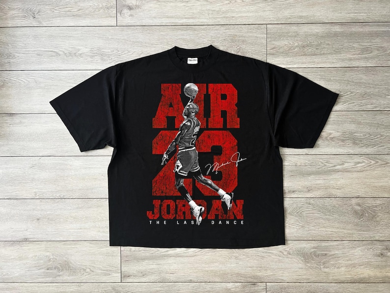 May include: Black t-shirt with a red graphic of a basketball player balancing a ball, with the words "AIR 23 JORDAN". The text "THE LAST DANCE" is below the player. The shirt has a crew neck and short sleeves.