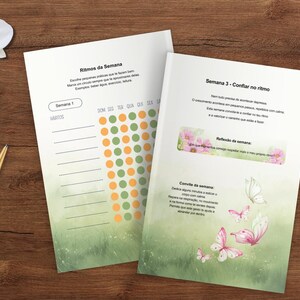 May include: Two open journals with text and colorful graphics rest on a wooden surface, alongside a gold pen and a sprig of white orchids. The journal pages feature text and a dot chart. One page has butterflies.