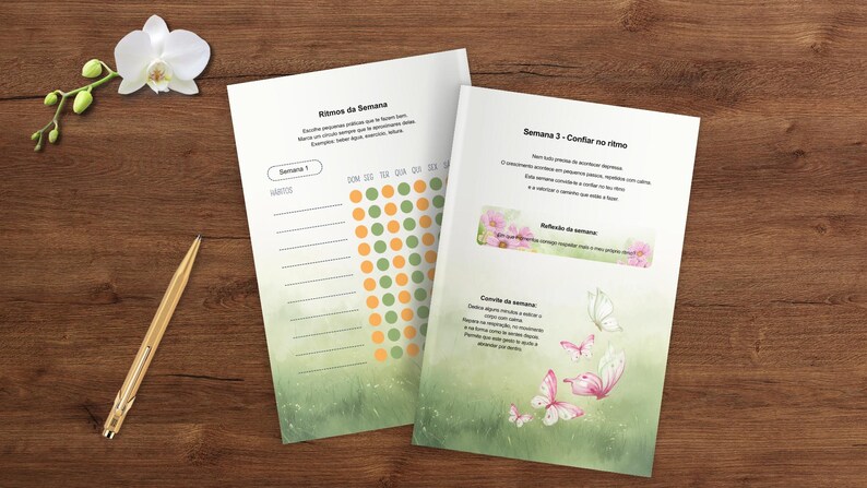 May include: Two open journals with text and colorful graphics rest on a wooden surface, alongside a gold pen and a sprig of white orchids. The journal pages feature text and a dot chart. One page has butterflies.