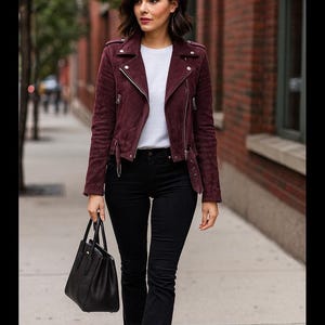 May include: A burgundy suede biker jacket with silver zippers, paired with a white t-shirt, black flared jeans, and a black handbag. The outfit is completed with black boots, creating a stylish, urban look.
