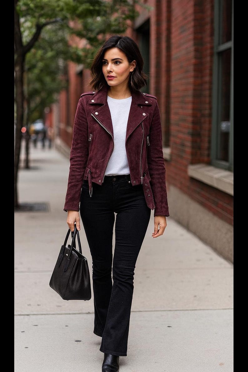 May include: A burgundy suede biker jacket with silver zippers, paired with a white t-shirt, black flared jeans, and a black handbag. The outfit is completed with black boots, creating a stylish, urban look.