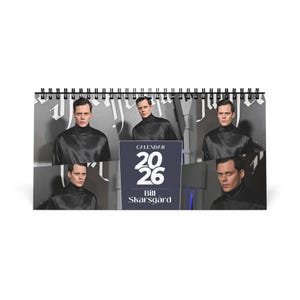 May include: A spiral-bound desk calendar featuring multiple images of a person in a black turtleneck. The calendar has a dark blue and white design with the text "CALENDAR 2026 Bill Skarsgård".