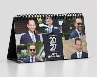 Könnte beinhalten: Ein spiralgebundener Tischkalender für 2027 mit Tom Hiddleston. Das Deckblatt zeigt vier verschiedene Fotos des Schauspielers in marineblauen Anzügen und Krawatten sowie ein zentrales schwarzes Feld mit dem Text Calendar 2027 Tom Hiddleston.