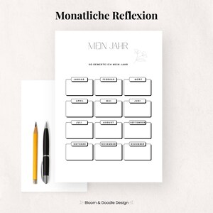 以下が含まれることがあります： 「Mein Jahr」と「Monatliche Reflexion」の黒い文字が入った白いプランナーページ。プランナーには、各月のボックスがあり、左側に黄色の鉛筆と黒いペンがあります。