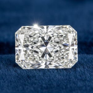 Könnte beinhalten: Ein loser Edelstein im Radiant-Schliff mit klarem, farblosem Aussehen und einer stark facettierten Oberfläche. Der Stein hat eine rechteckige Form mit abgeschrägten Ecken und zeigt komplexe geometrische Lichtreflexionen.