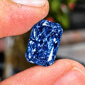 Könnte beinhalten: Ein rechteckig geschliffener Edelstein in tiefem Blau mit einer stark facettierten Oberfläche, die ein komplexes, schimmerndes Muster aus hellen und dunklen blauen Reflexionen erzeugt und eine brillante, intensive Sättigung zeigt.