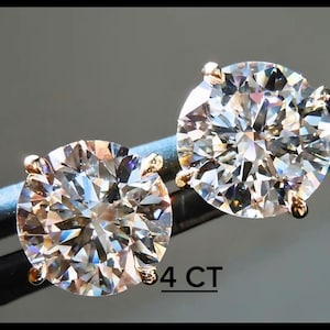 Könnte beinhalten: Ein Paar funkelnde Diamant-Ohrstecker. Die rund geschliffenen Diamanten sind in Goldzargen gefasst und werden von einer Pinzette gehalten. Der Text "4 CT" ist sichtbar.