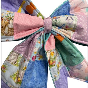 May include: A large, colorful fabric bow featuring a patchwork design. The bow incorporates various pastel colors, including pink, blue, purple, and green. The fabric is decorated with Easter-themed patterns, such as bunnies and floral motifs, creating a festive and decorative item.